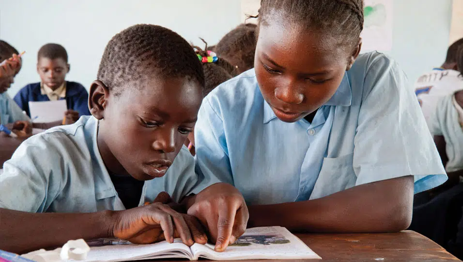 A young boy reading with an older girl, supported by Project Luangwa.